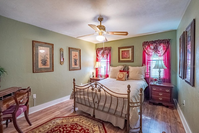 bedroom with a textured wall, wood finished floors, a ceiling fan, and baseboards