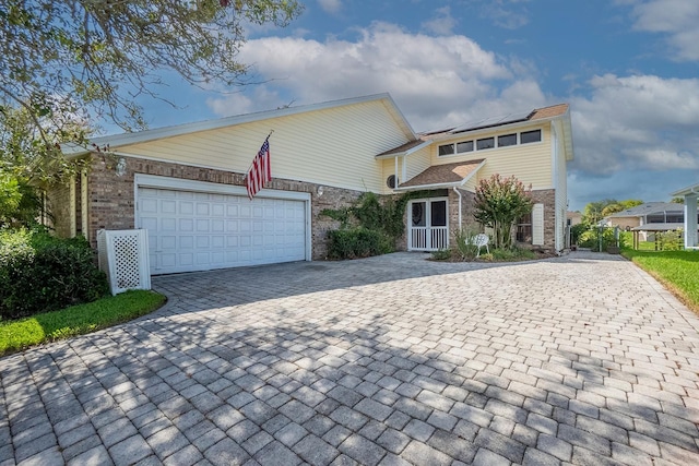 view of front facade featuring decorative driveway, brick siding, roof mounted solar panels, and an attached garage