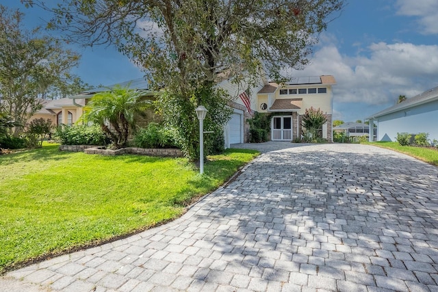 view of front facade with a front lawn, decorative driveway, roof mounted solar panels, and an attached garage