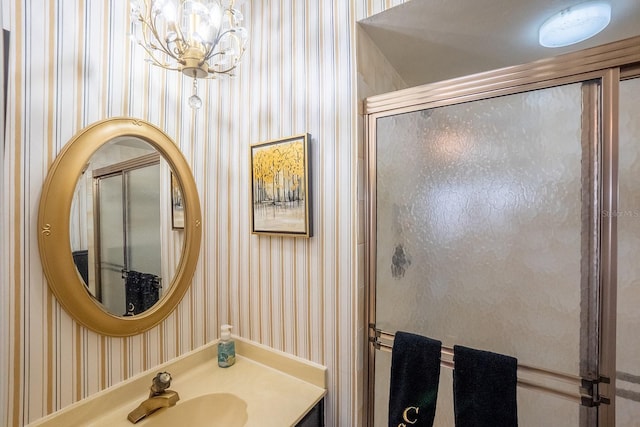 bathroom featuring a notable chandelier, a shower with door, a sink, and wallpapered walls