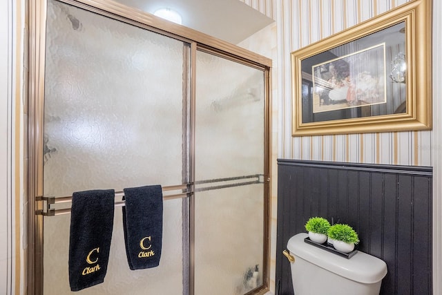 bathroom with toilet, a shower with door, and wallpapered walls