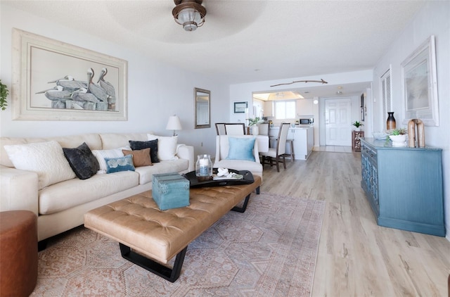 living room featuring a textured ceiling, light wood-type flooring, and ceiling fan