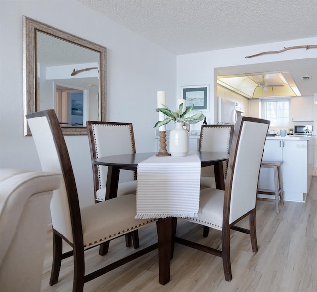 dining space with ceiling fan, light hardwood / wood-style floors, and a textured ceiling