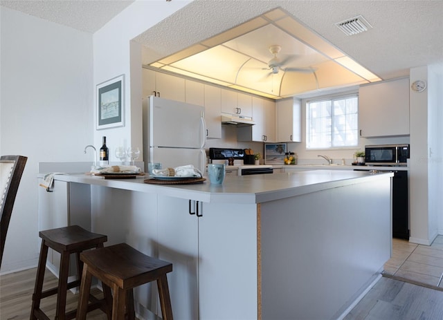 kitchen featuring a breakfast bar, white refrigerator, light wood-type flooring, a textured ceiling, and black range with electric cooktop