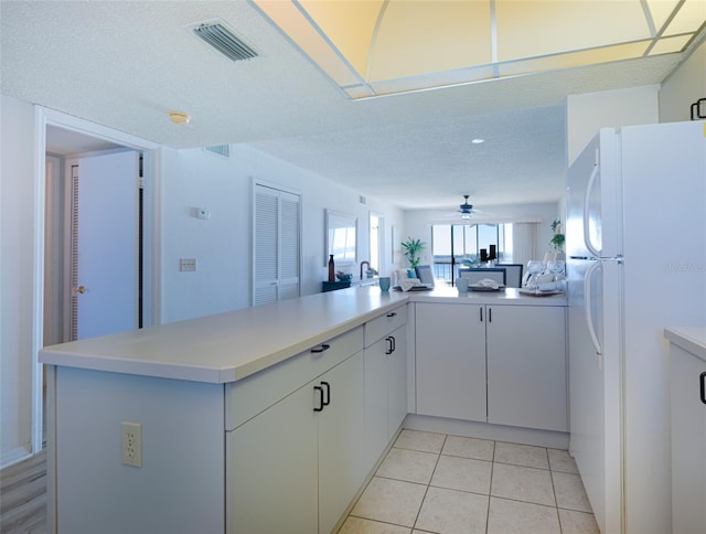 kitchen with kitchen peninsula, a textured ceiling, ceiling fan, white fridge, and white cabinetry