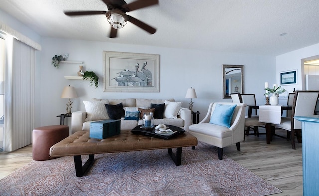 living room featuring ceiling fan, light hardwood / wood-style flooring, and a textured ceiling