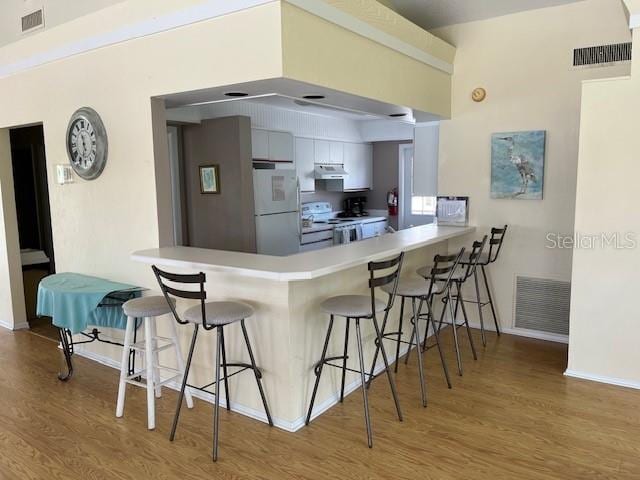 kitchen featuring kitchen peninsula, a breakfast bar, white appliances, hardwood / wood-style floors, and white cabinetry