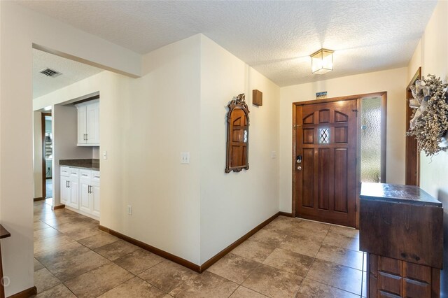 foyer entrance with a textured ceiling and light tile patterned flooring