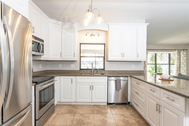 kitchen with pendant lighting, appliances with stainless steel finishes, white cabinets, a sink, and dark stone counters