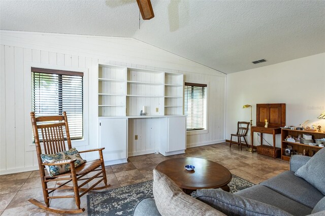 living room featuring visible vents, wood walls, vaulted ceiling, a textured ceiling, and ceiling fan