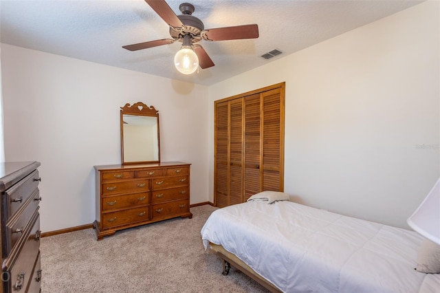 bedroom featuring ceiling fan, light colored carpet, a closet, and a textured ceiling