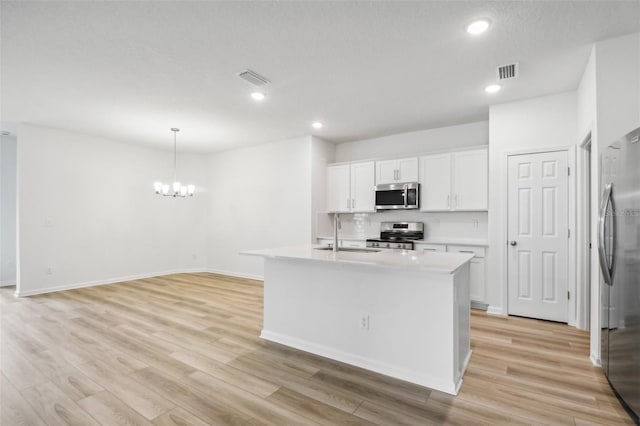 kitchen featuring sink, stainless steel appliances, pendant lighting, a kitchen island with sink, and white cabinets