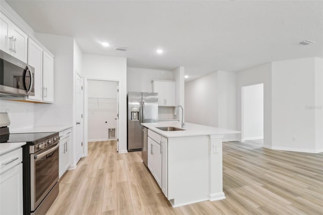 kitchen with white cabinetry, sink, stainless steel appliances, light hardwood / wood-style floors, and a center island with sink