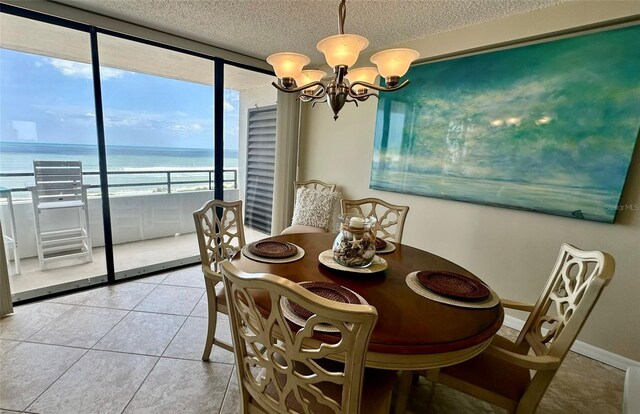 dining room featuring expansive windows, an inviting chandelier, a textured ceiling, a water view, and light tile patterned floors