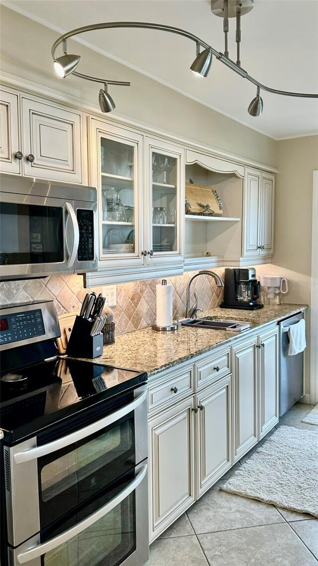 kitchen featuring tasteful backsplash, light tile patterned floors, sink, rail lighting, and stainless steel appliances