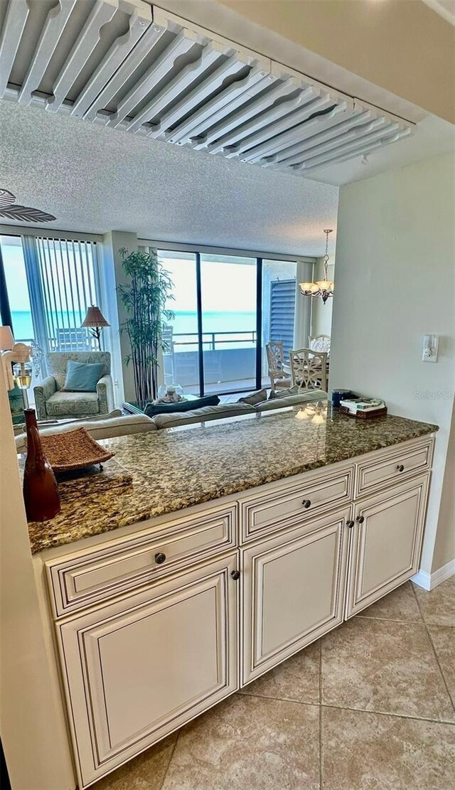 kitchen featuring cream cabinets, stone countertops, light tile patterned flooring, and a chandelier