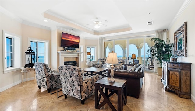 tiled living room featuring ceiling fan, a fireplace, a tray ceiling, and ornamental molding