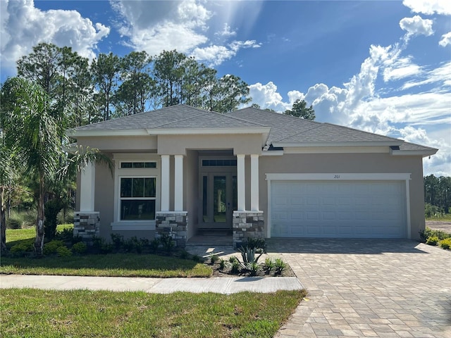 prairie-style house featuring a garage, stone siding, decorative driveway, and stucco siding