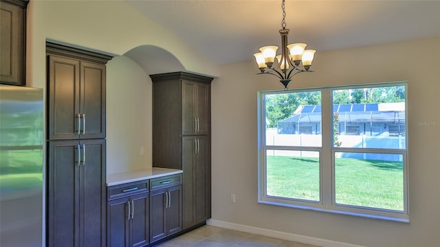 kitchen featuring lofted ceiling, stainless steel refrigerator, dark brown cabinetry, decorative light fixtures, and a chandelier