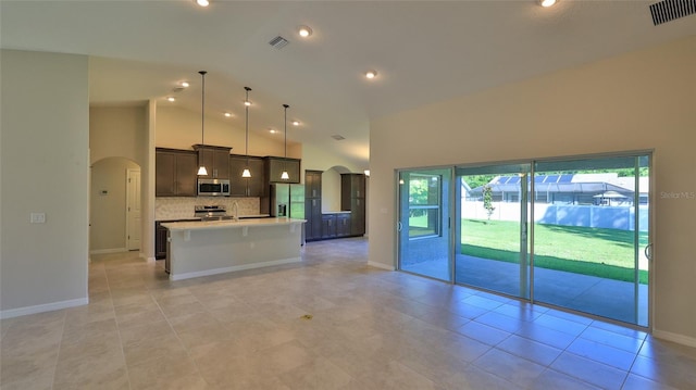 kitchen with decorative light fixtures, high vaulted ceiling, an island with sink, stainless steel appliances, and backsplash