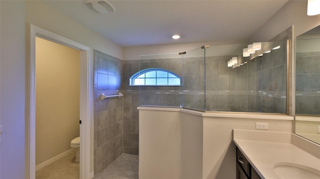 bathroom with tiled shower, vanity, toilet, and tile patterned flooring