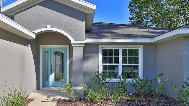 property entrance featuring a shingled roof and stucco siding