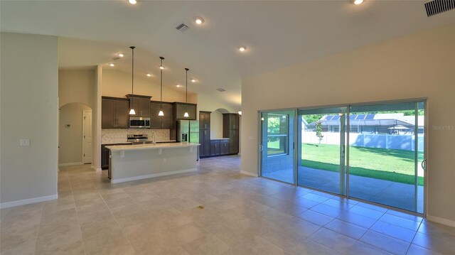 kitchen featuring appliances with stainless steel finishes, pendant lighting, high vaulted ceiling, tasteful backsplash, and a kitchen island with sink