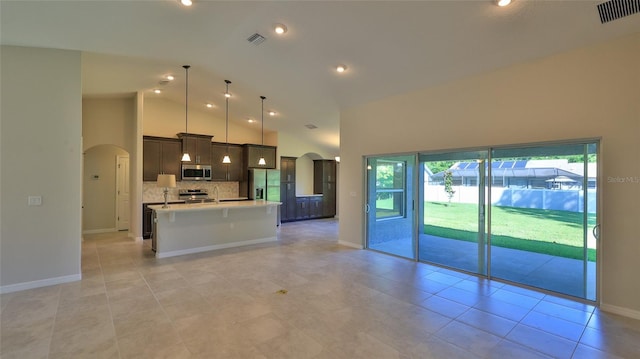 kitchen with high vaulted ceiling, a center island with sink, appliances with stainless steel finishes, pendant lighting, and decorative backsplash