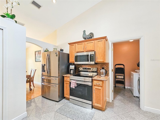 kitchen featuring tasteful backsplash, high vaulted ceiling, light tile patterned flooring, appliances with stainless steel finishes, and washer and dryer