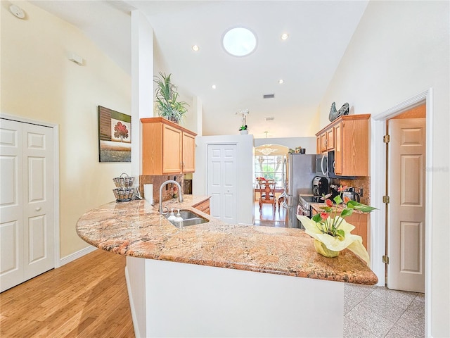 kitchen with sink, appliances with stainless steel finishes, high vaulted ceiling, light stone counters, and kitchen peninsula