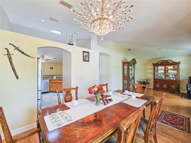 dining space with vaulted ceiling, sink, ceiling fan with notable chandelier, and light hardwood / wood-style flooring