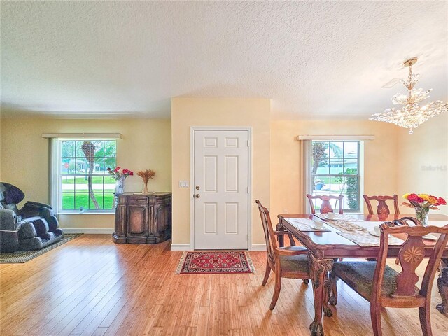 dining room featuring light wood-type flooring, a textured ceiling, a wealth of natural light, and an inviting chandelier