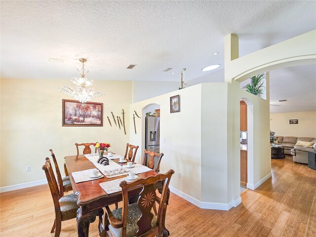 dining area with a notable chandelier, a textured ceiling, light wood-type flooring, and lofted ceiling