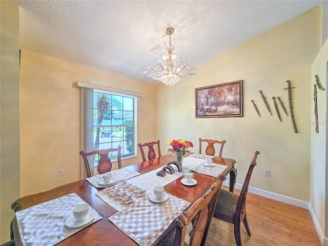 dining room with lofted ceiling, light wood-type flooring, a textured ceiling, and a chandelier