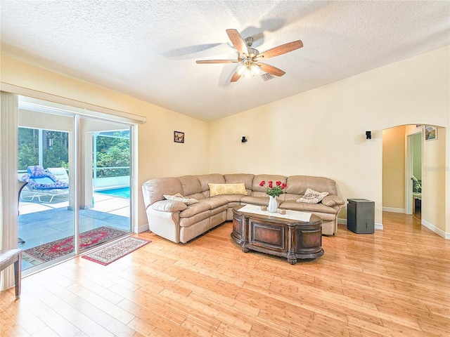 living room with ceiling fan, a textured ceiling, and light wood-type flooring