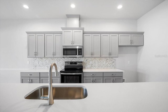 kitchen with appliances with stainless steel finishes, backsplash, sink, and gray cabinetry