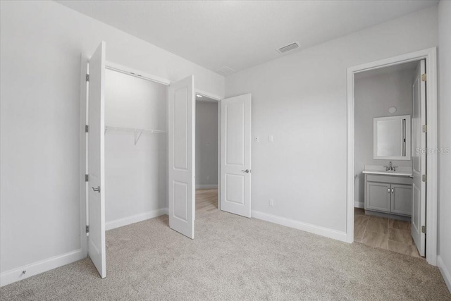 unfurnished bedroom featuring ensuite bath, sink, light carpet, and a closet