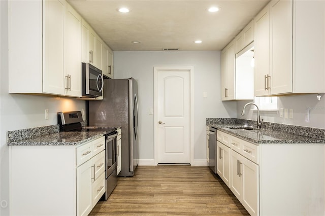 kitchen featuring sink, light hardwood / wood-style flooring, appliances with stainless steel finishes, white cabinets, and dark stone counters