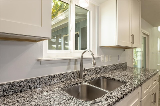 kitchen with a healthy amount of sunlight, dark stone counters, sink, and white cabinets