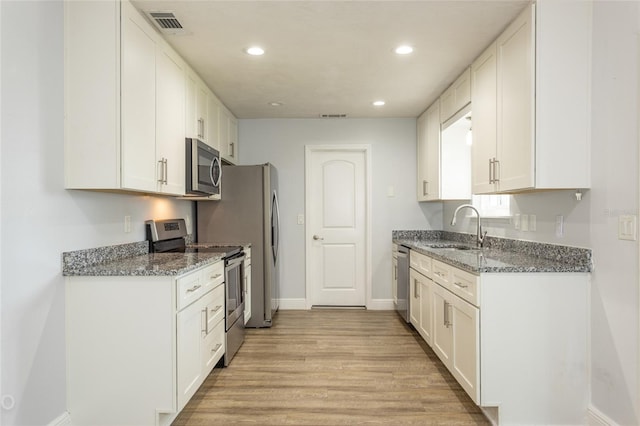 kitchen featuring appliances with stainless steel finishes, white cabinetry, sink, dark stone counters, and light hardwood / wood-style floors