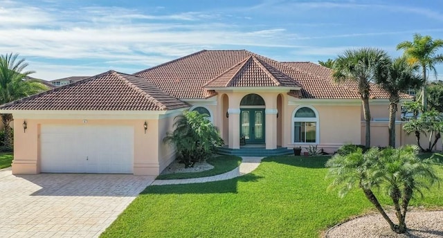 mediterranean / spanish-style home featuring decorative driveway, stucco siding, an attached garage, a tiled roof, and a front lawn