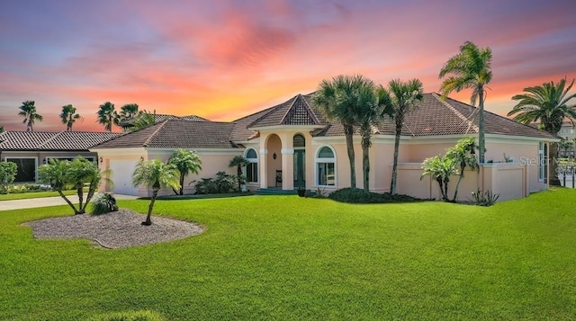 mediterranean / spanish home with an attached garage, stucco siding, a tile roof, and a yard