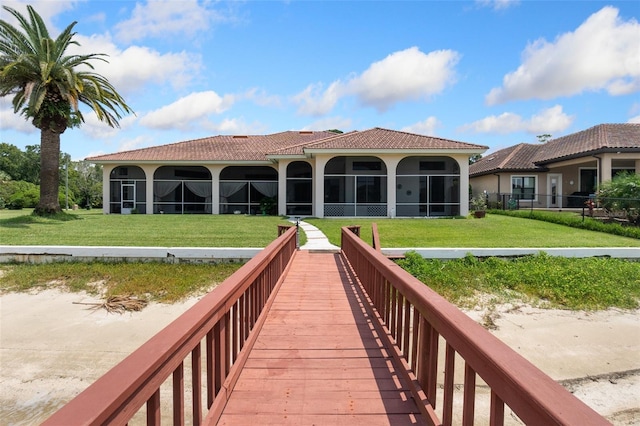 rear view of property featuring stucco siding, a tiled roof, a sunroom, and a yard