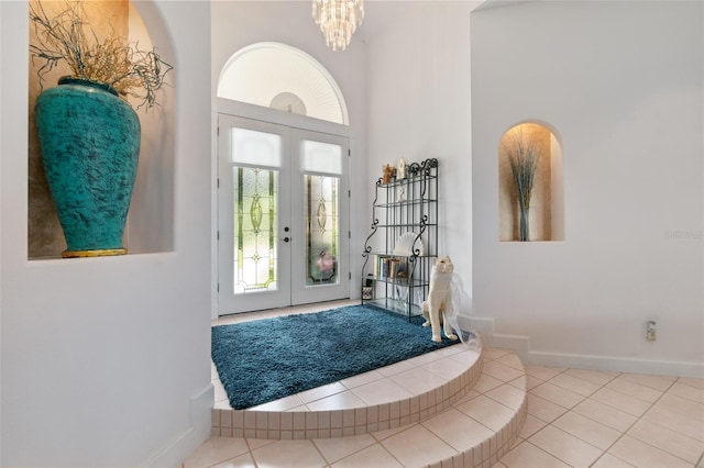 foyer featuring french doors, a towering ceiling, a chandelier, tile patterned flooring, and baseboards