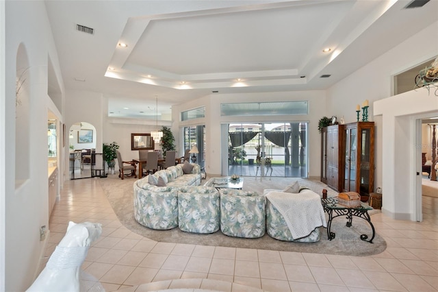 living room with a tray ceiling, visible vents, and light tile patterned flooring