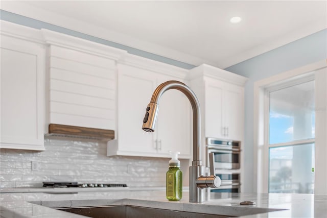 details featuring light stone counters, backsplash, stainless steel double oven, white cabinetry, and a sink