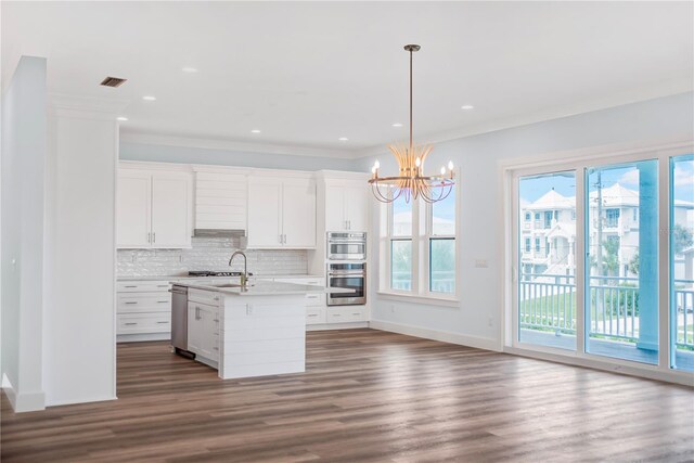 kitchen with hardwood / wood-style floors, ornamental molding, white cabinetry, hanging light fixtures, and a center island with sink