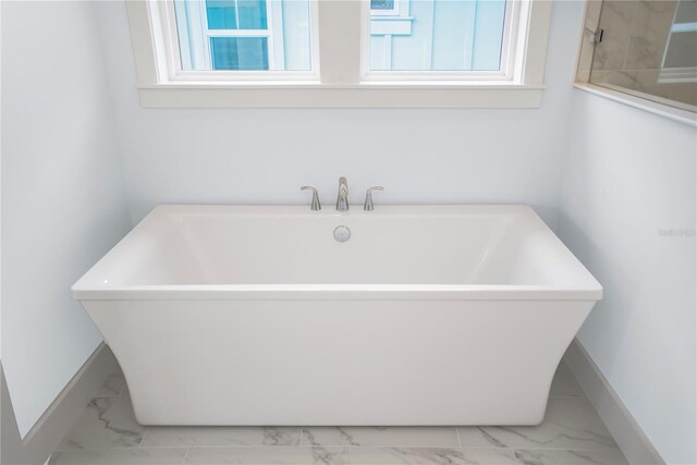 bathroom featuring marble finish floor, a freestanding tub, and baseboards
