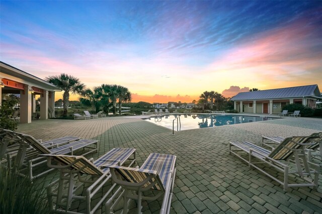 pool at dusk featuring a community pool and a patio