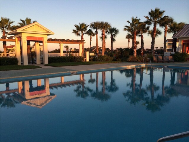 pool at dusk featuring a pergola